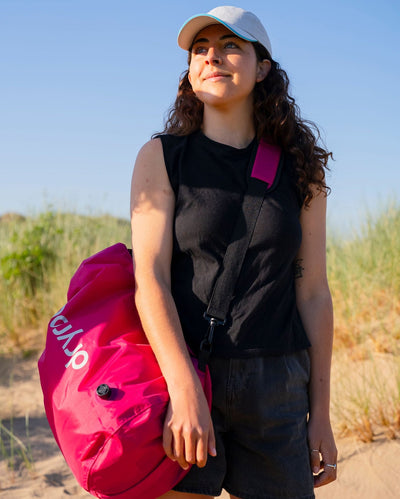 Woman on beach carrying hot pink Dryrobe® compression bag 