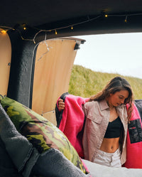 Camo Grey dryrobe® Cushion Cover on bed of a campervan, next to a woman stood in doorway 