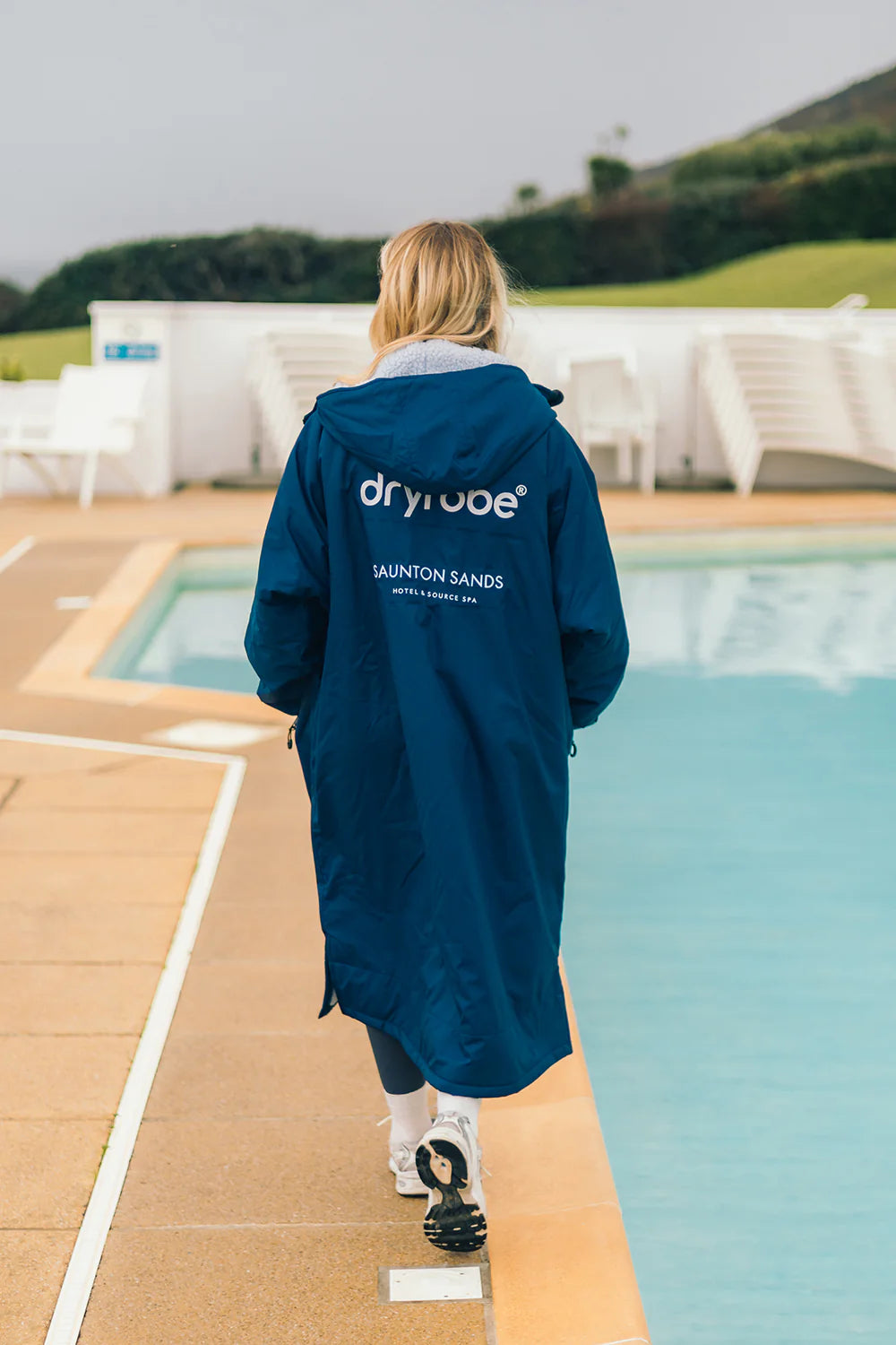 Person wearing a blue Dryrobe® change robe by a poolside