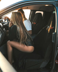 Man and woman sat in front seats of van, using dryrobe Van Seat Cover in Black