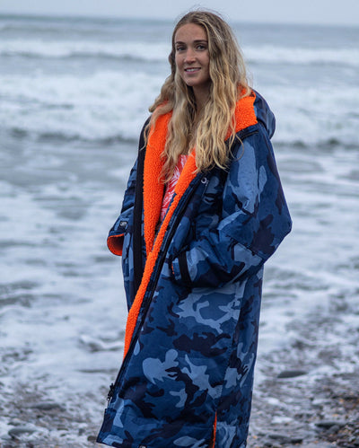 Woman stood in front of sea, wearing Blue Camo Orange dryrobe advance long sleeve changing robe 
