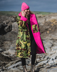 Woman walking on a beach wearing Camo Pink dryrobe® Advance Long Sleeve and Pink dryrobe® Eco Beanie