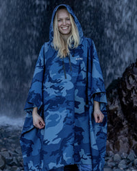 Woman stood infront of waterfall smiling, wearing  Blue Camo dryrobe® Waterproof Poncho with hood up 