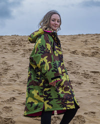 Girl smiling at camera walking on beach, wearing Camo Pink dryrobe® Advance Kids Long Sleeve