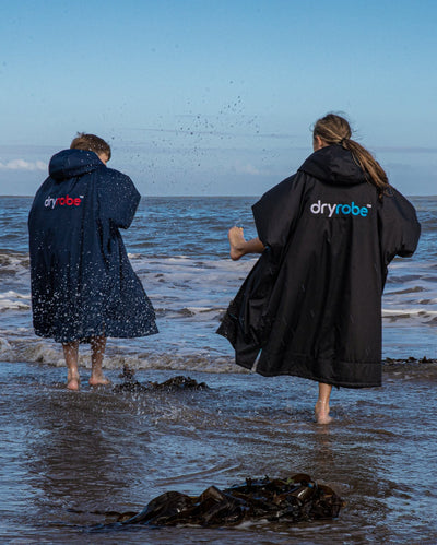 Two kids splashing in the shoreline, wearing dryrobe® Advance Kids Long Sleeve