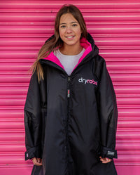 Girl stood in front of pink door, wearing Black Pink dryrobe® Advance Kids Long Sleeve