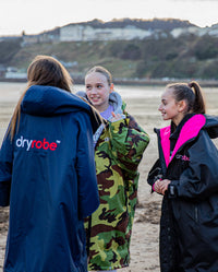 Three girls chatting on the beach, wearing Kids dryrobe Advance change robes