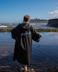 Boy stood on beach with back to the camera wearing Black Blue dryrobe® Advance Kids Short Sleeve changing robe