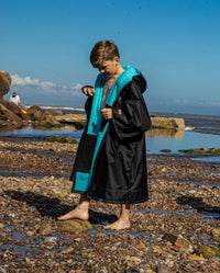 Boy walking along beach wearing Black Blue dryrobe® Advance Kids Short Sleeve changing robe unzipped