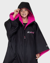 Girl wearing Black Pink dryrobe® Advance Kids Short Sleeve changing robe with hood up