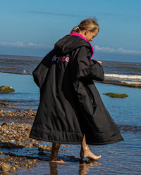 Girl stood by the sea wearing Black Pink dryrobe® Advance Kids Short Sleeve changing robe