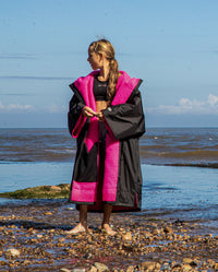 Girl stood in front of the sea looking to the left, wearing Black Pink dryrobe® Advance Kids Short Sleeve changing robe