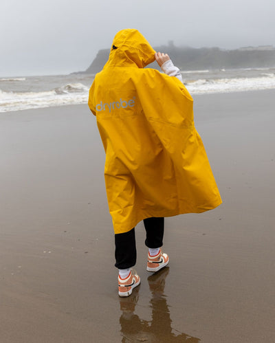 Girl walking away from camera on a beach, wearing Yellow Kids dryrobe® Waterproof Poncho