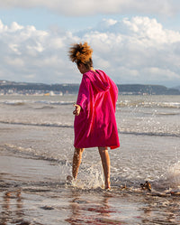 Girl running through the shoreline at the beach, wearing Kids Towel Robe in Pink