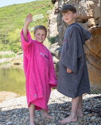 Two boys stood next to a lake, one of them waving, both wearing Kids Towel Robes