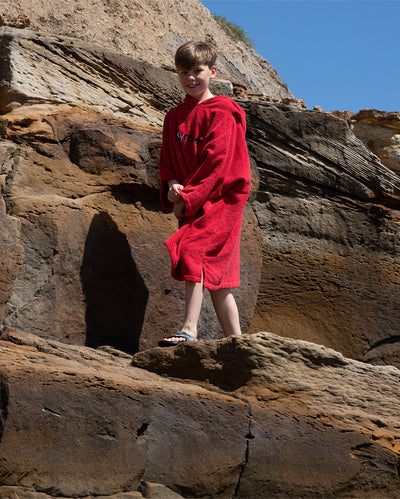 Boy walking along rocks, wearing Red Kids Organic Towel robe