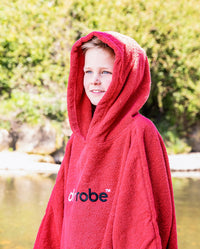 Boy stood in front of river, wearing Red Kids Organic Towel robe with hood up 