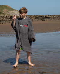 Boy stood on the beach pointing at the sky, wearing Kids Towel Robe in Slate Grey