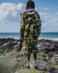 *MALE* standing on a beach facing the sea, wearing Camo Grey dryrobe® Advance  