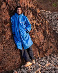 *MALE* leaning on rock on a beach,  wearing Cobalt Blue Black dryrobe® Advance Long Sleeve