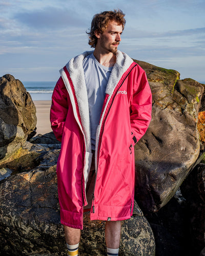 **MALE** Man stood in the sun in front of beach, wearing dryrobe Advance long sleeve changing robe in Pink Light Grey