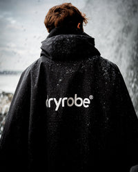 *MALE* stood in the rain with back to the camera, wearing Black dryrobe® Adults Waterproof Poncho