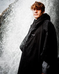 *MALE* stood next to waterfall facing camera, wearing Black dryrobe® Waterproof Poncho 