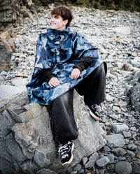 *MALE* sat on a beach, wearing  Blue Camo dryrobe® Waterproof Poncho  