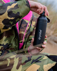 Person sat in sand dunes, taking lid off of dryrobe Ocean Bottle