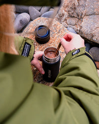 Person sat on beach stirring hot chocolate in dryrobe Ocean Bottle Brew Flask