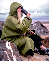 Woman sat on beach wearing dryrobe Advance Long Sleeve changing robe, sipping from dryrobe Ocean Bottle Brew Flask