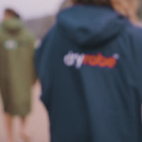 Group of adults wearing long sleeve Dryrobe® Advance changing robes whilst walking on the beach 