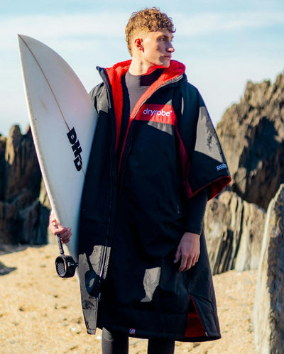Adult male on beach wearing Dryrobe® Black red remix