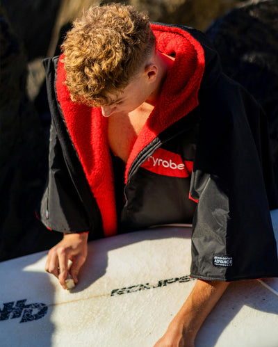 Adult male with surfboard wearing Dryrobe® Black red remix