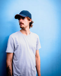 *MALE* Man looking off to the left leaning against a blue wall, wearing Deep Sea Blue dryrobe Quick Dry Cap