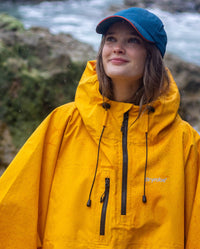 Woman stood in the rain on a beach looking up, wearing Deep Sea Blue dryrobe Quick Dry Cap and Yellow Waterproof Poncho