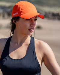 Woman stood on a beach, wearing Orange dryrobe Quick Dry Cap