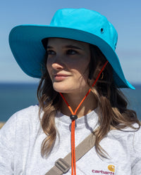 Woman stood in front of the sea smiling, wearing dryrobe Quick Dry Brim Hat in Blue