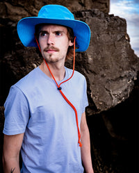 *MALE* Man stood in front of rocks on a beach, wearing dryrobe® Quick Dry Brimmed Hat in Blue