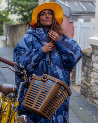 Woman stood in street next to bicycle, wearing Yellow dryrobe Quick Dry Brimmed Hat and dryrobe Advance in Blue Camo